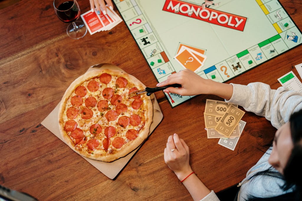 Casual game night featuring Monopoly, pepperoni pizza, and red wine on a wooden table.
